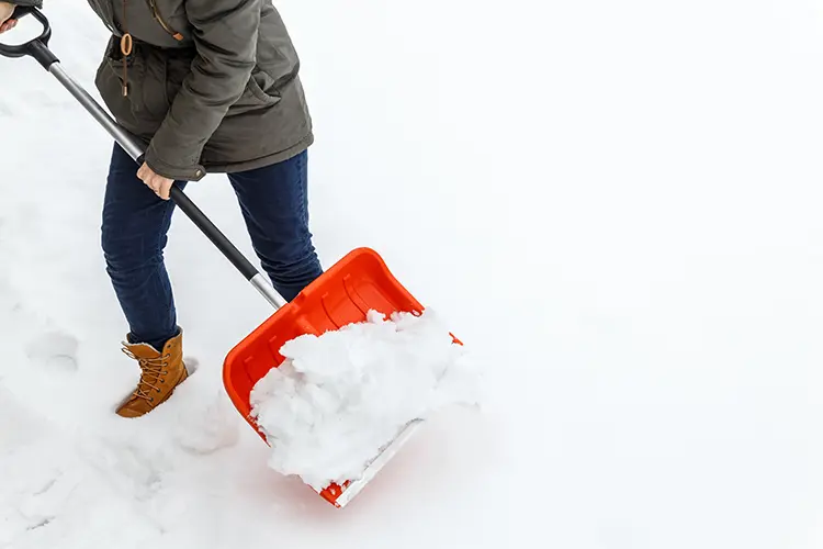 Eine Person schippt Schnee mit einem orangenen Schneeschieber